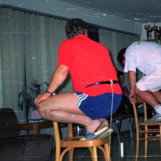 People play a game balancing bottles on chairs indoors.