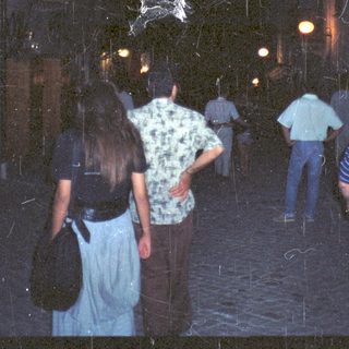 People walking under a dark, arched passageway with a statue.