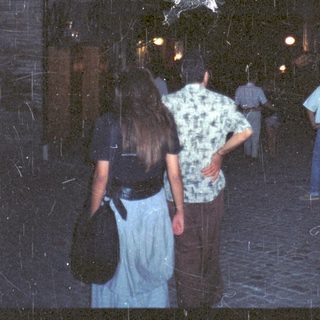 People walking under a dark, arched passageway with a statue.