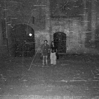 Couple stands on a street with arched doorways at night.