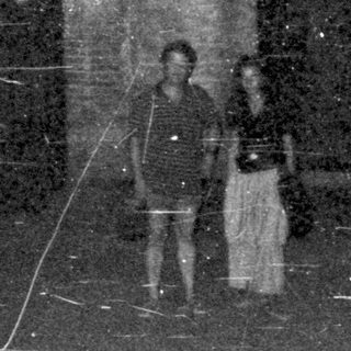 Couple stands on a street with arched doorways at night.