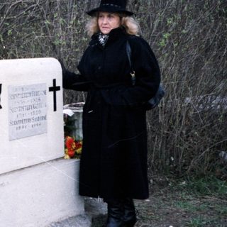Here's a brief summary of the image: Women stand at a gravesite with flowers and a memorial.