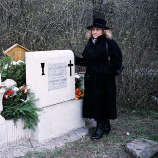 Here's a brief summary of the image: Women stand at a gravesite with flowers and a memorial.