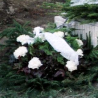 Here's a brief summary of the image: Women stand at a gravesite with flowers and a memorial.