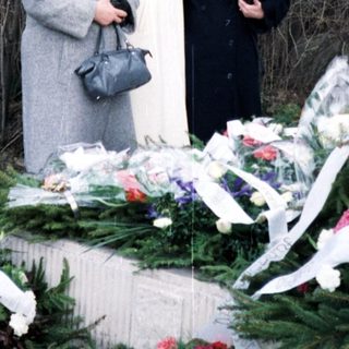 Here's a brief summary of the image: Women stand near a grave adorned with flowers.