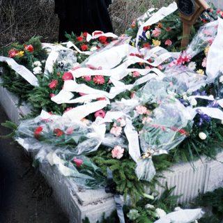 Woman stands near a grave adorned with flowers and plaque.