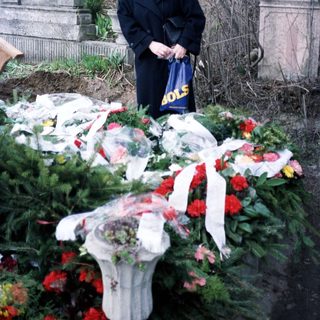 Woman stands near a grave covered with flowers.