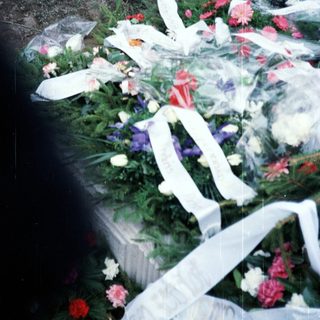Floral tributes and ribbons adorn a grave or memorial.