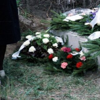 People visit a gravesite with a cross and flowers.