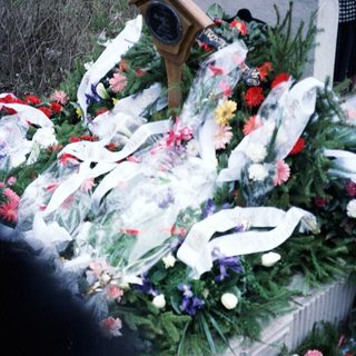 Here's a brief summary of the image: Grave adorned with flowers, ribbons, and a plaque.