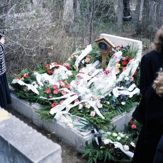 Grave covered with flowers and ribbons in a wooded area.