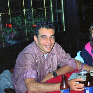 Two people sit at a table with drinks outdoors.