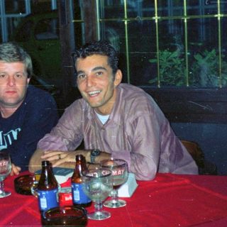 Two men sit at a table with drinks at night.