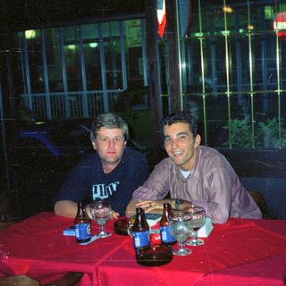 Two men sit at a table with drinks at night.
