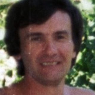 Man stands shirtless on a balcony, holding a beer.