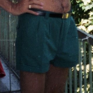 Man stands shirtless on a balcony, holding a beer.