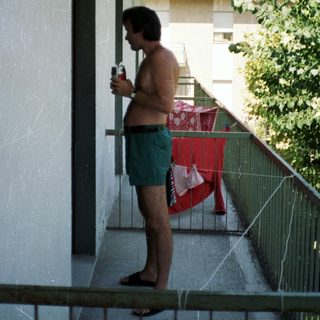 Man stands on balcony holding a drink, laundry drying.