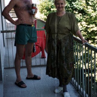 Man and woman stand on a balcony, relaxing outdoors.