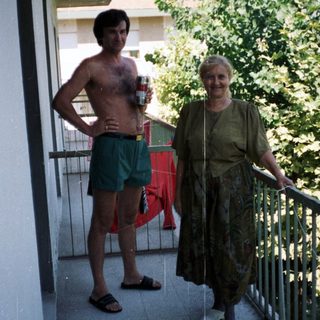 Man and woman stand on a balcony, relaxing outdoors.