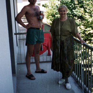 Man and woman stand on a balcony, relaxing outdoors.