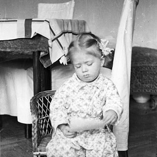 Here's a brief summary of the image: Young girl kneeling, wearing a floral patterned outfit.