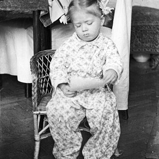 Here's a brief summary of the image: Young girl kneeling, wearing a floral patterned outfit.