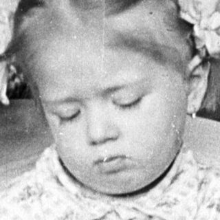 Here's a brief summary of the image: Young girl kneeling, wearing a floral patterned outfit.
