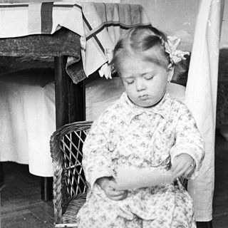 Here's a brief summary of the image: Young girl kneeling, wearing a floral patterned outfit.