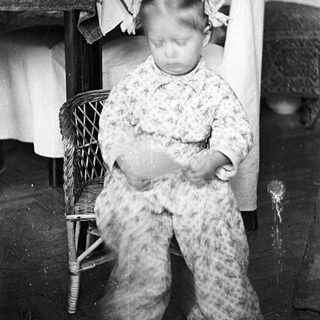 Here's a brief summary of the image: Young child seated on a chair, blurry motion.