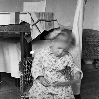 Child in pajamas sits, reading, near a bed.