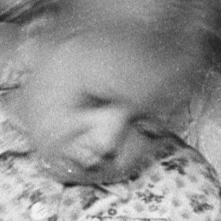 Child in pajamas sits, reading, near a bed.