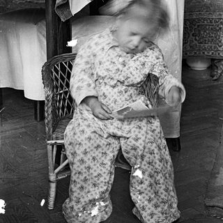 Child in pajamas sits, reading, near a bed.