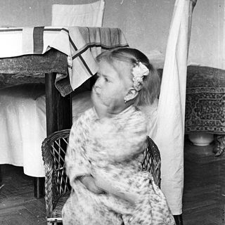 Here's a brief summary of the image: Girl in patterned pajamas sits on a wicker chair.