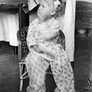 Here's a brief summary of the image: Girl in patterned pajamas sits on a wicker chair.