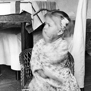 Here's a brief summary of the image: Girl in patterned pajamas sits on a wicker chair.