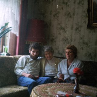 Three people sit on a couch in a lived-in room.