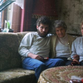 Three people sit on a couch in a lived-in room.