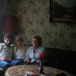Three people sit on a couch in a lived-in room.