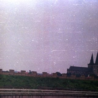 Castle and walls overlooking a river under a hazy sky.