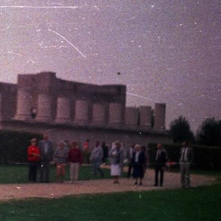Ruins of a classical monument with people walking nearby.