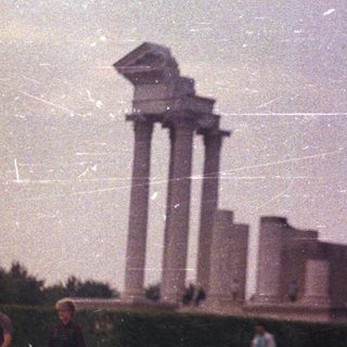 Ruins of a classical monument with people walking nearby.