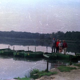 People stand near a lake with rowboats.