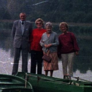 People stand near a lake with rowboats.