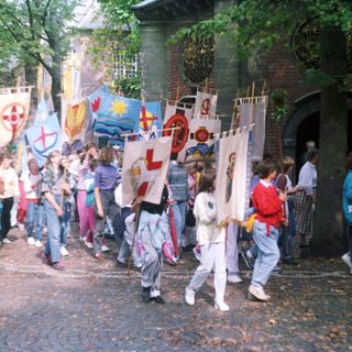 Children parade with flags in front of a brick building.