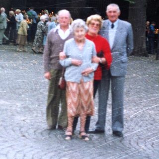 Elderly couple and man pose outdoors near a building.