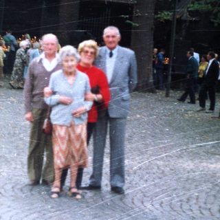 Elderly couple and man pose outdoors near a building.