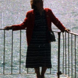 Woman stands looking at a lake and mountain range.