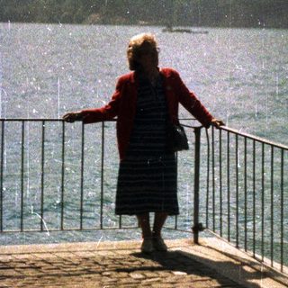 Woman stands looking at a lake and mountain range.