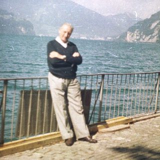Man stands on a patio overlooking a lake and mountains.