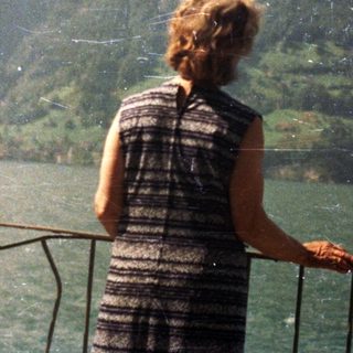 Person overlooking a lake with mountains and green slopes.